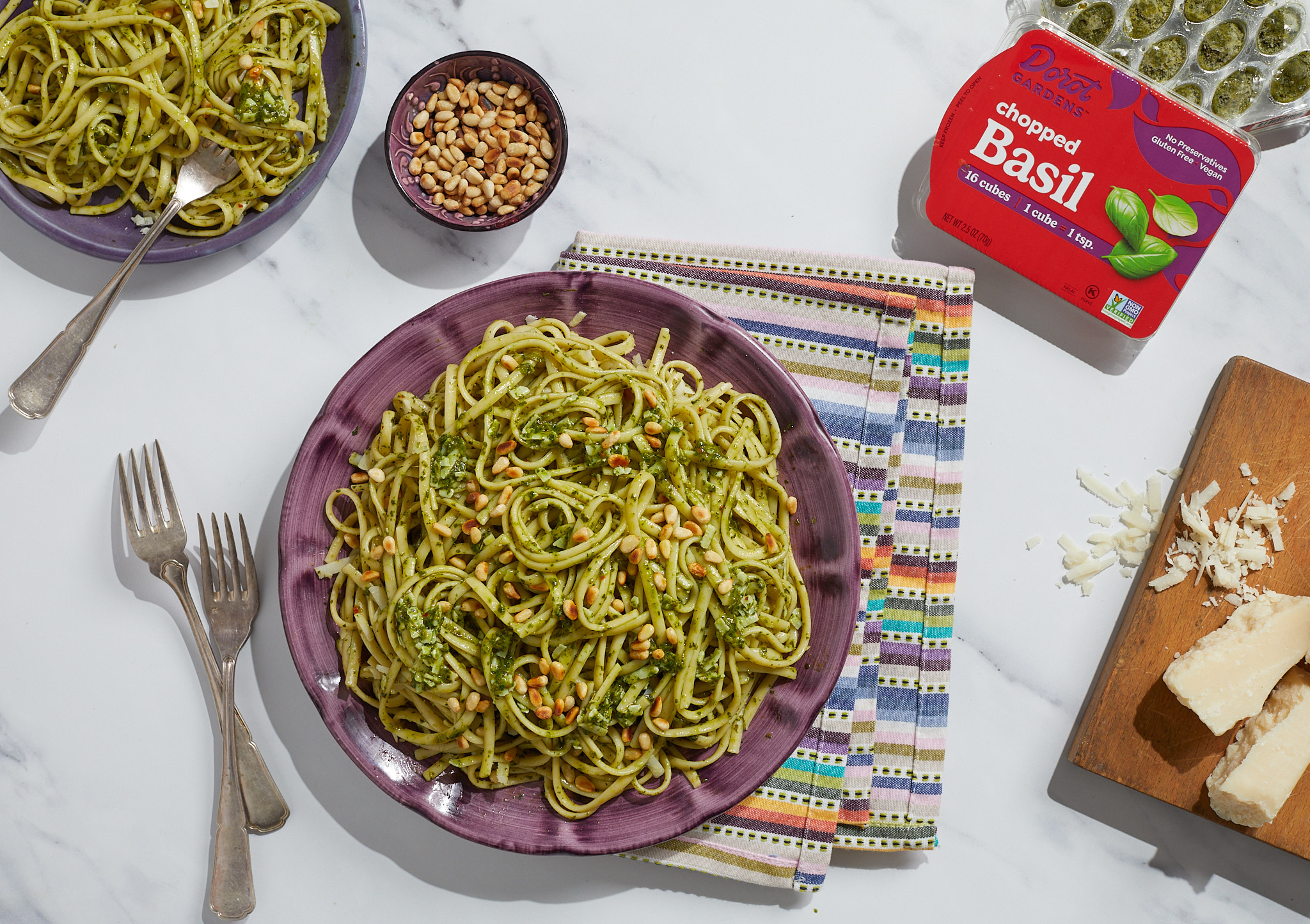 Pesto pasta in a bowl with a Dorot basil pack, nuts, and cheese on a board.