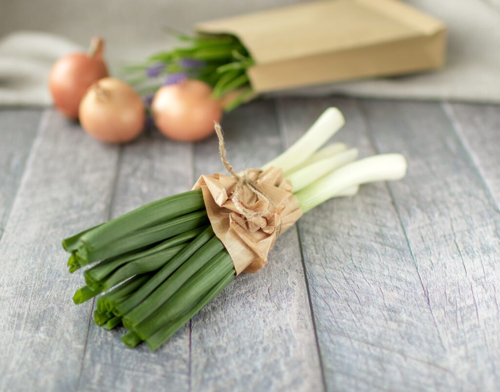 A bundle of fresh leeks and onions on a rustic wooden surface, ideal for cooking inspiration.